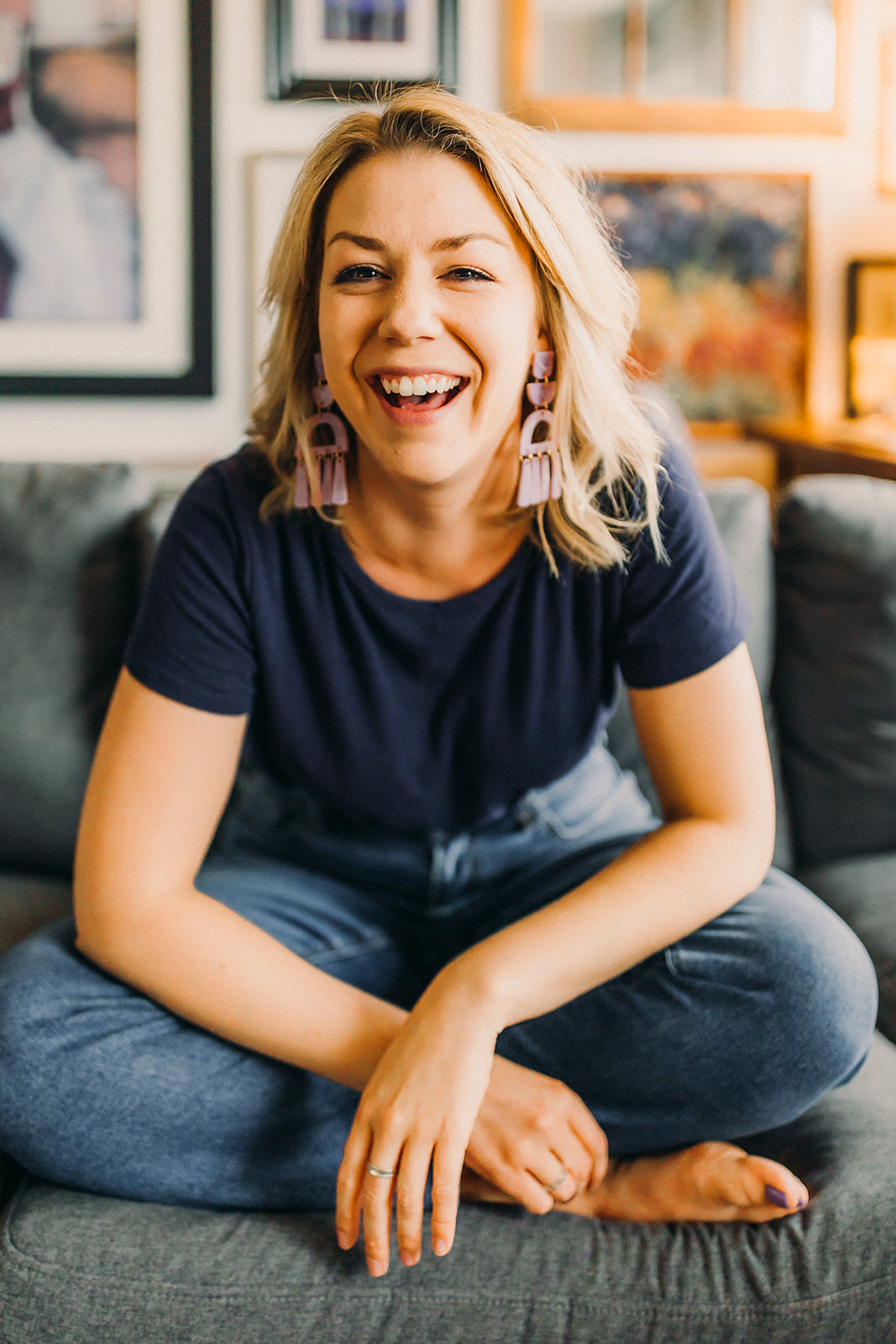 Lauren Hughes sits cross-legged on a couch laughing.